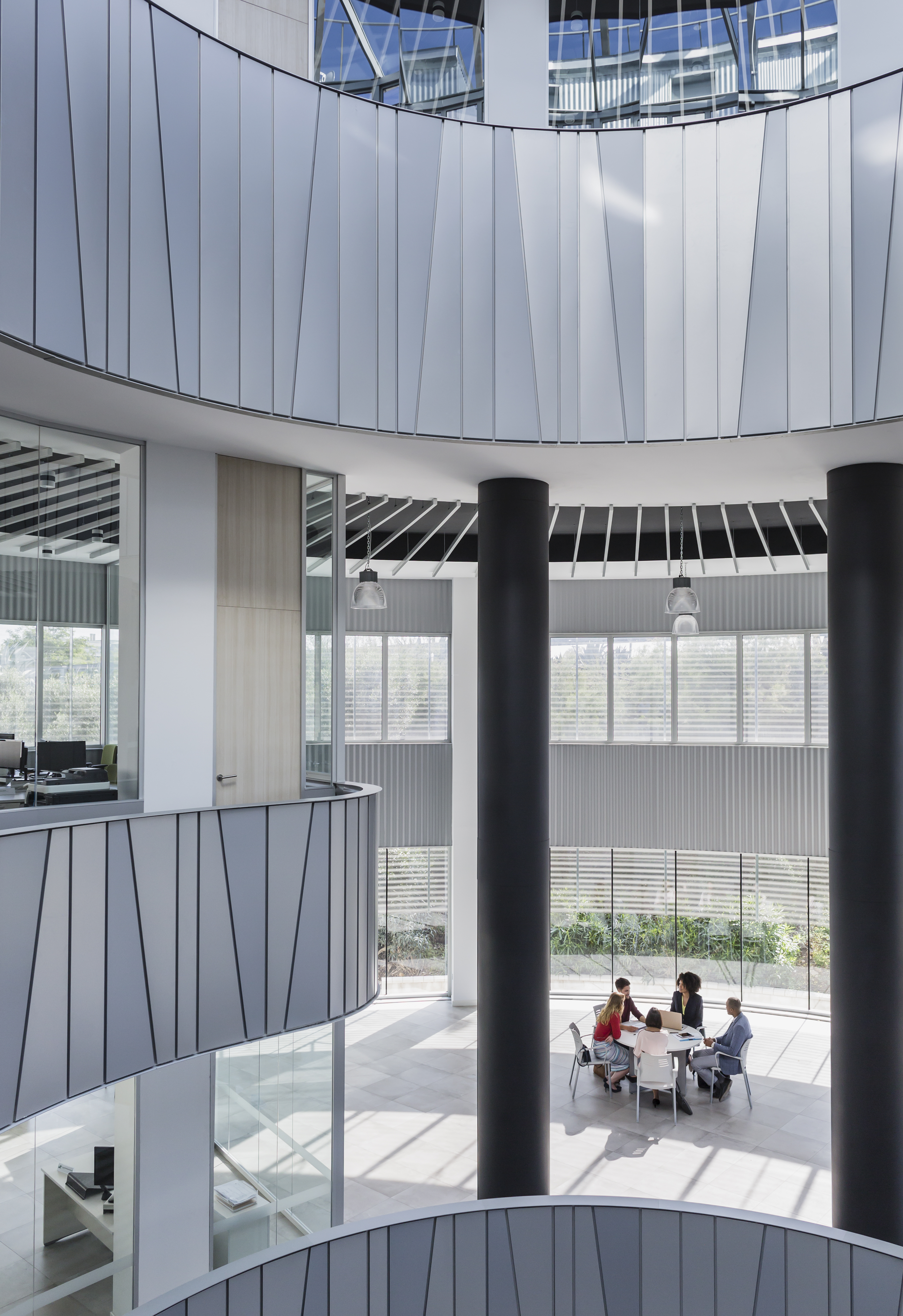 Business professionals meet around a table in a bright, architectural office atrium with open space and natural light—symbolizing collaboration, innovation, and contemporary workplace design.
